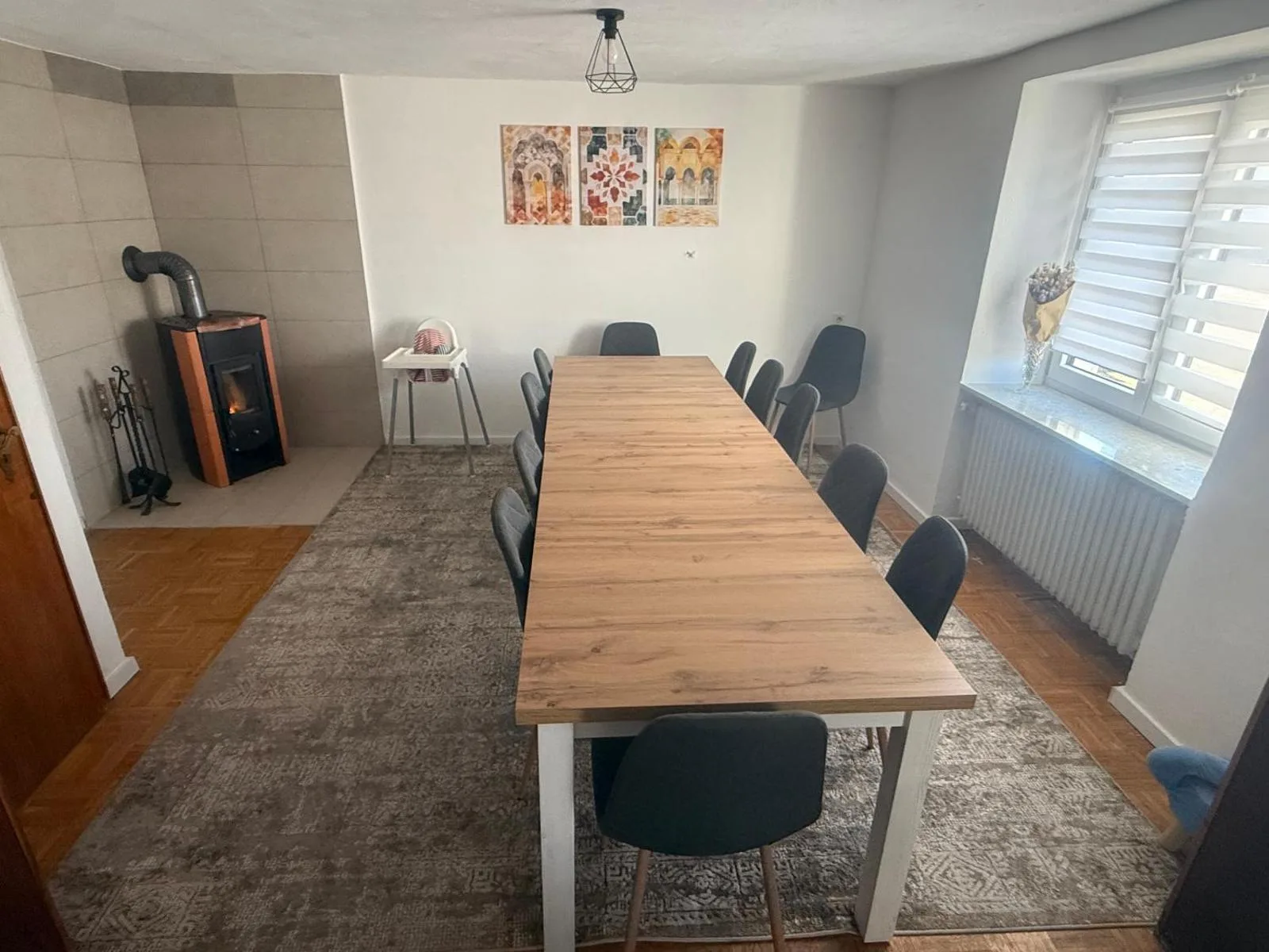 Langer Esstisch mit dunklen Stühlen für bis zu zehn Personen, im Hintergrund Kaminofen und Babyhochstuhl, orientalische Wandbilder.