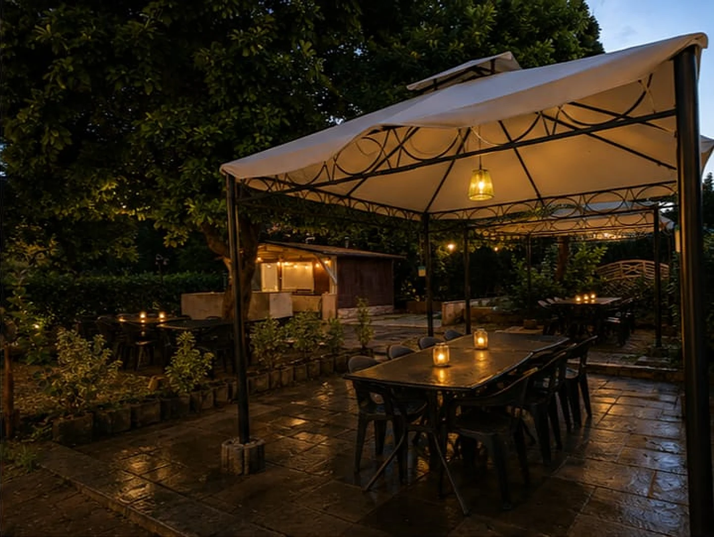 Pavillon mit langer Tafel für die ganze Gruppe, Windlichter auf dem Tisch, im Hintergrund die Außenküche