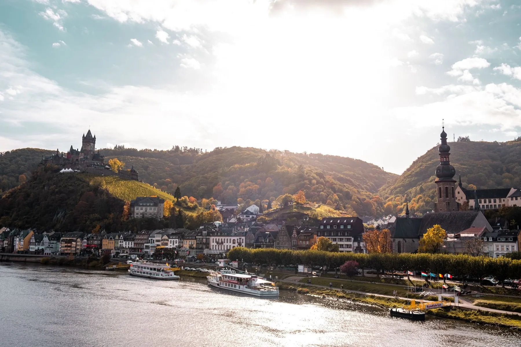 Moselort im herbstlichen Gegenlicht mit Burg über der Stadt
